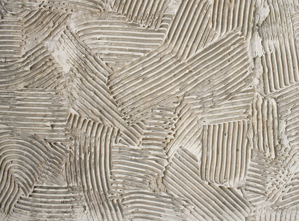 Superficie de mortero de aislamiento térmico con surcos marcados y acabado beige, mostrando la textura aplicada en franjas cruzadas sobre el revestimiento.