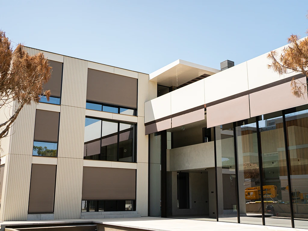 Edificio moderno con grandes ventanales y persianas enrollables en la fachada.