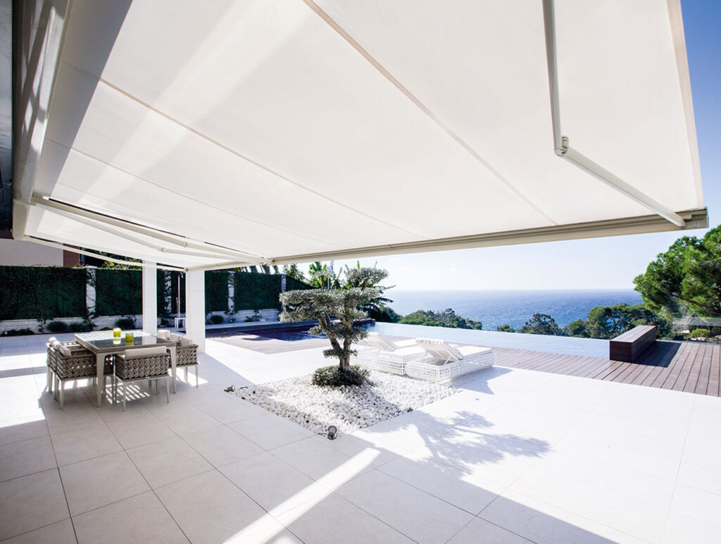 Toldo retráctil instalado en una terraza con vista al mar, proporcionando sombra en un ambiente exterior.