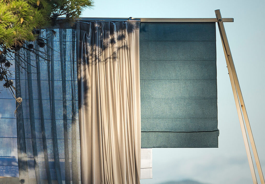 Cortinas de tela en tonos azules y beige colgadas en un soporte exterior con un fondo claro.