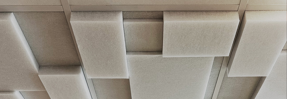Techo modular con paneles acústicos beige y blancos dispuestos en distintos niveles, creando un patrón geométrico limpio y luminoso.