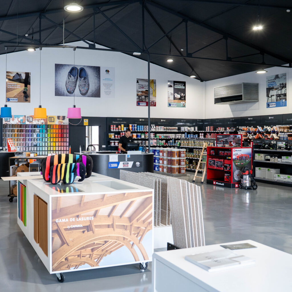 Interior de una tienda de bricolaje con estanterías llenas de productos y un mostrador central de atención al cliente.